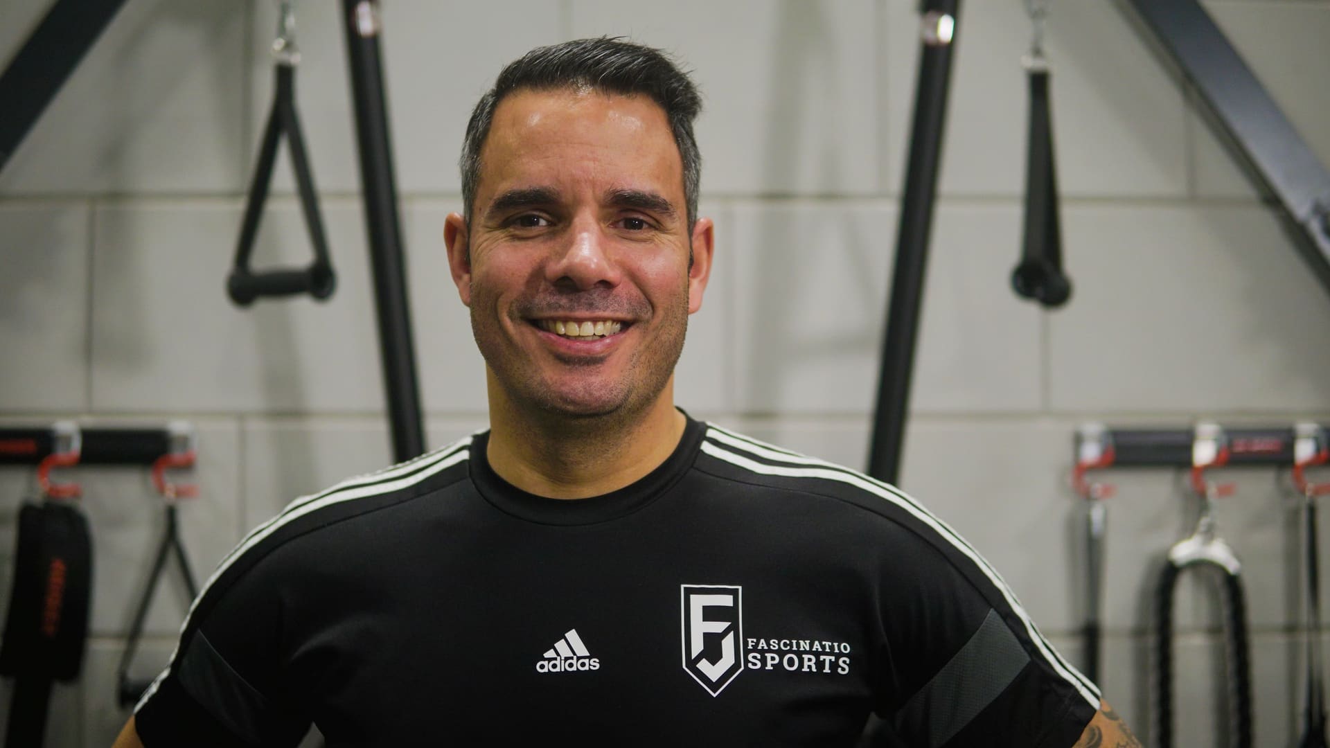 Trainer van Fascinatio Sports in de trainingszaal, met het clublogo op zijn shirt